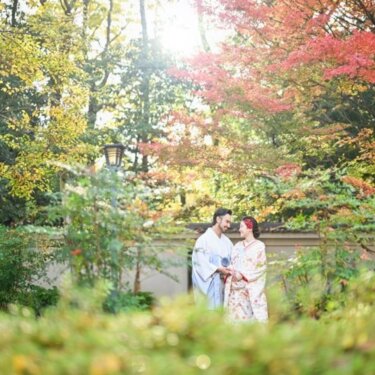 藤田邸跡庭園の紅葉と緑の庭園で見つめ合う、水色の着物姿の花婿と花柄着物姿の花嫁