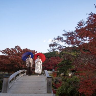 紅葉の橋の上で、紺と朱色の和傘を差す新郎新婦