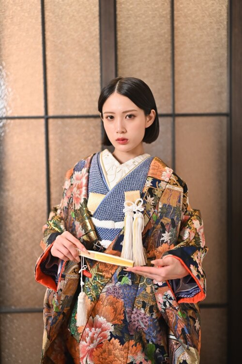 白扇を手に、オレンジと紺の花柄振袖姿で佇む花嫁のクローズアップ
