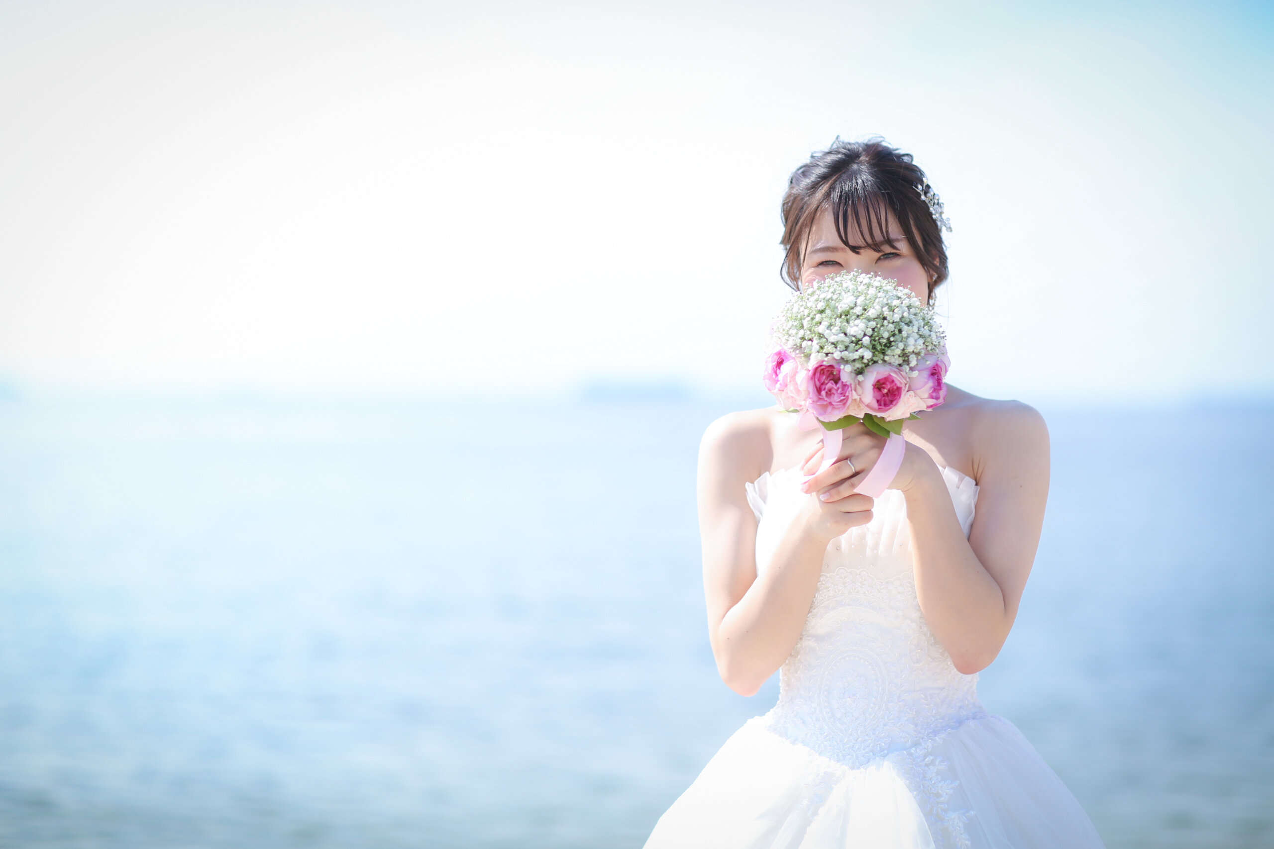 白とピンクのブーケで顔を隠す花嫁、りんくうビーチの海を望む透明感あふれる一枚