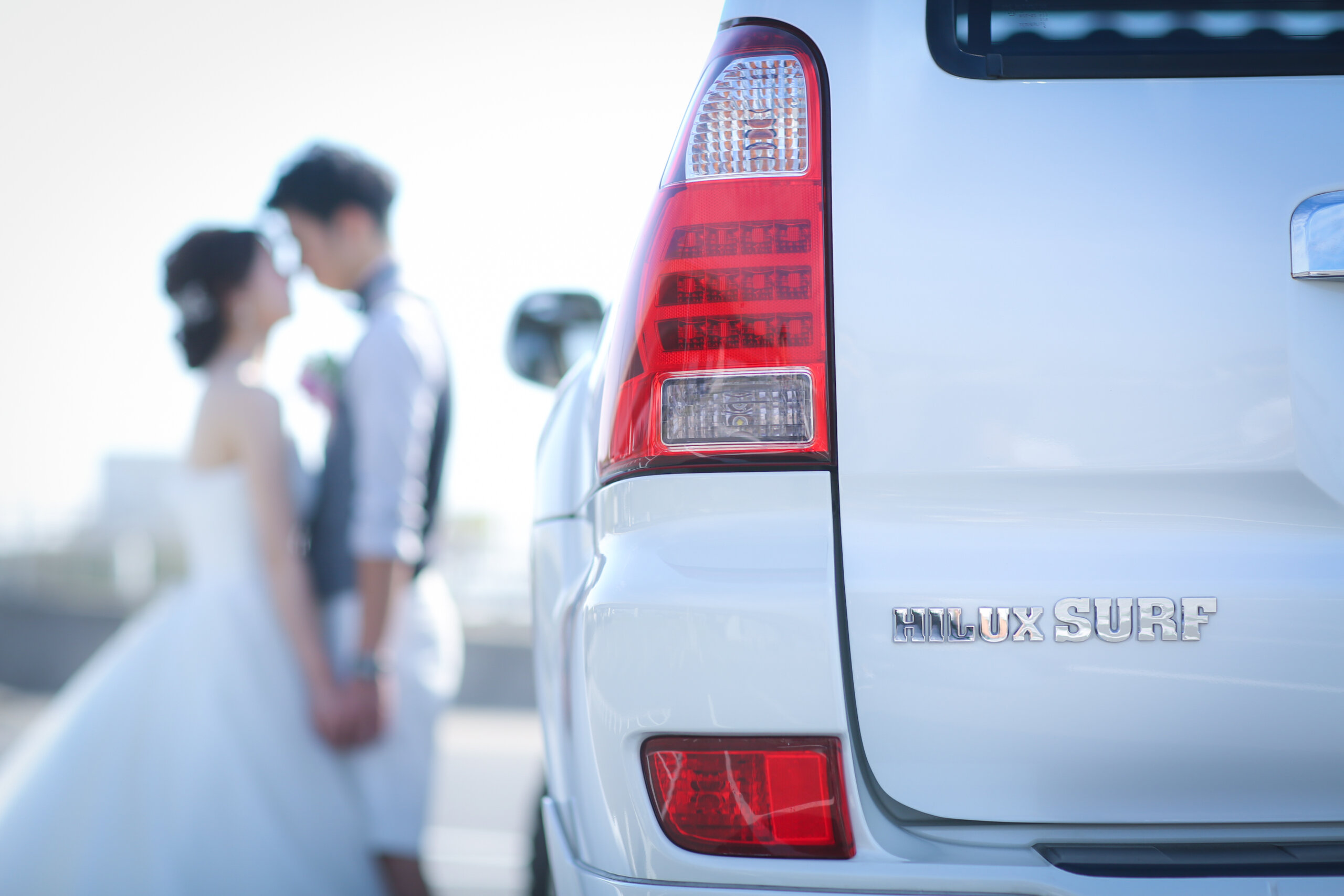 車のテールランプ越しに寄り添う新郎新婦、りんくうビーチのオフショット