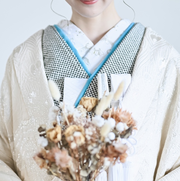 水色の縁取りが入った白い掛下姿で、ドライフラワーのブーケを抱く花嫁の胸元