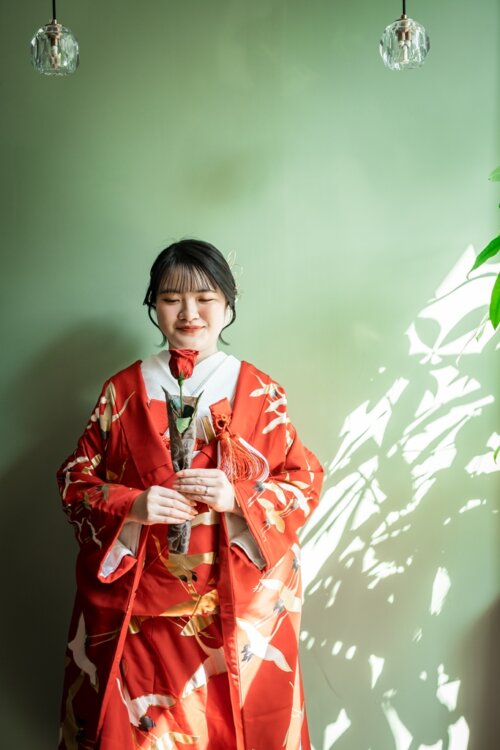 赤地に鶴が舞う色打掛をまとい、緑の壁に落ちる木漏れ日の中でやわらかく微笑む花嫁。和装のフォトウェディング