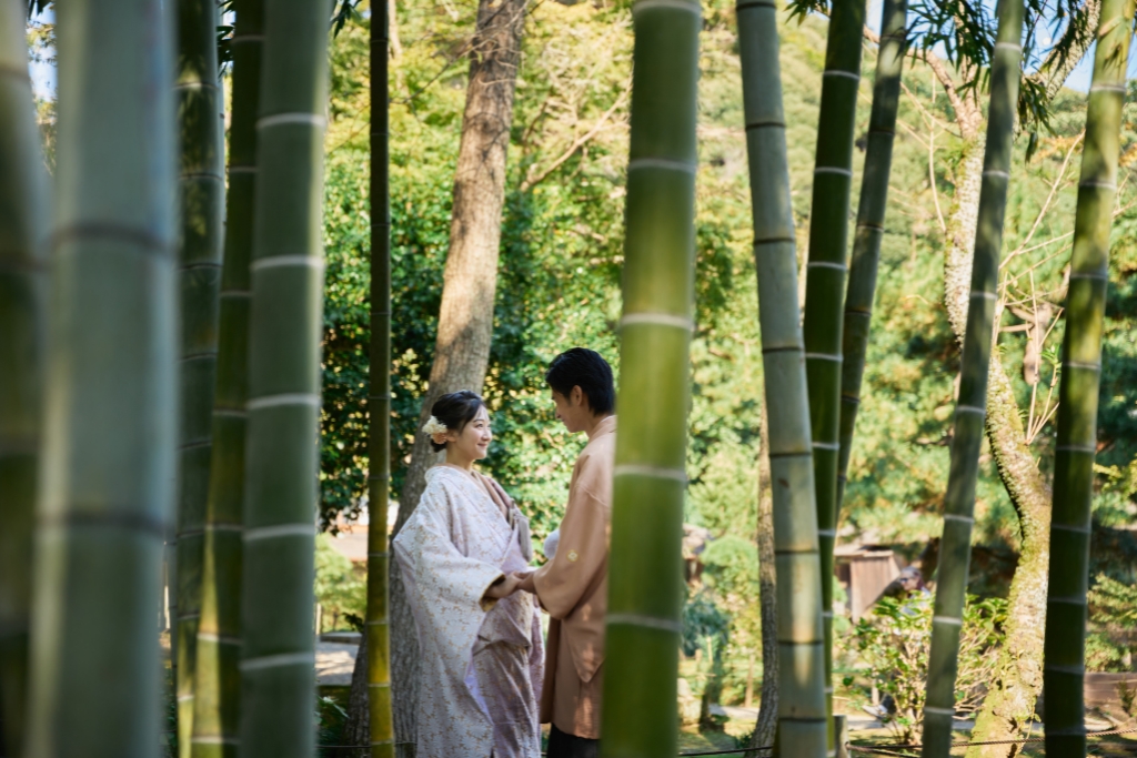 竹林越しに手をつなぎ見つめ合う薄橙の羽織袴の新郎と白地の着物姿の新婦