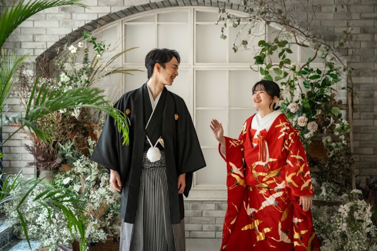 白レンガのアーチと花々を背に笑い合う新郎新婦。紋付袴と赤い色打掛で叶える結婚写真の前撮り