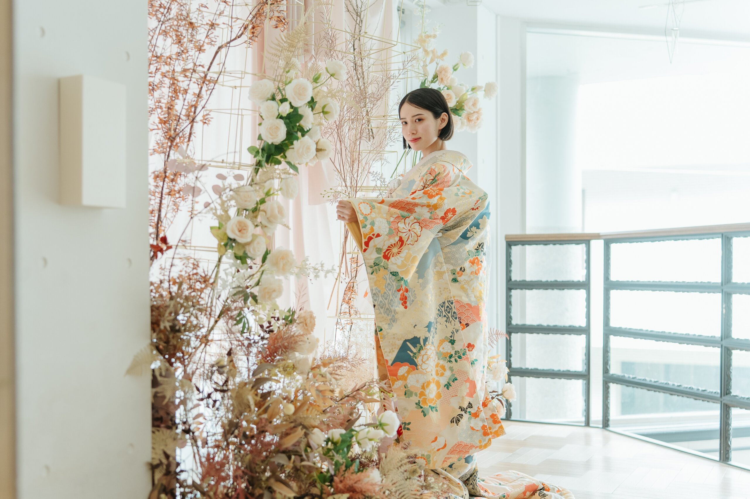 白いローズとドライフラワーの装花に囲まれた明るい空間で、青海波と花柄の色打掛を広げて振り返る花嫁。南青山店ラウンジスタジオでの和装前撮り