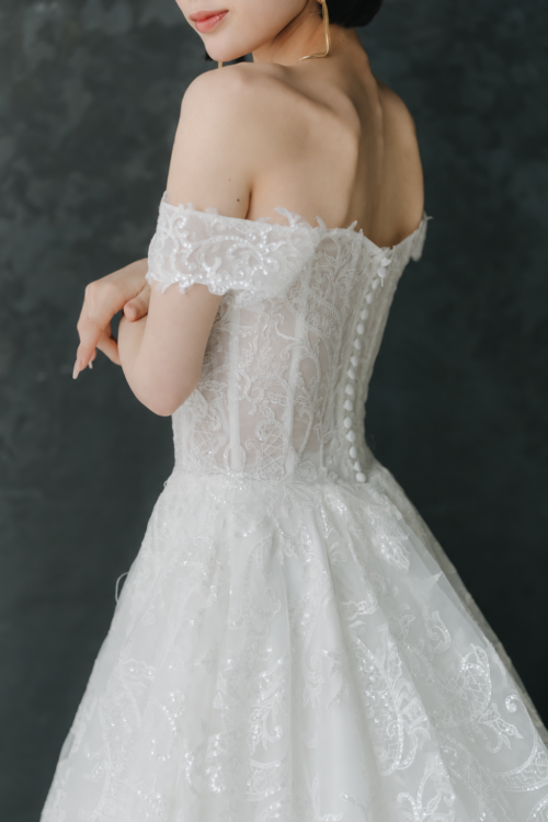 オフショルダーの袖と背中のくるみボタンを写したウェディングドレスのバックスタイル。前撮りで映える繊細なレース