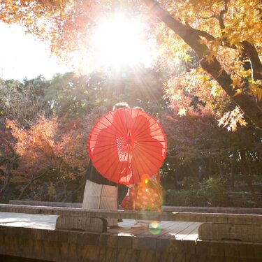 紅葉の木の下の木橋で赤い和傘に隠れて寄り添う和装の新郎新婦。秋の紅葉と撮る和装前撮りフォトウェディング