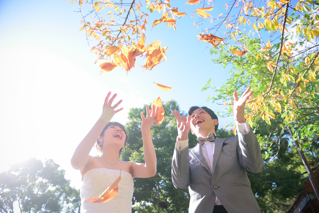落ち葉が舞う中でほほえむ新郎新婦。秋の前撮りで人気の落ち葉のシャワーを使った演出
