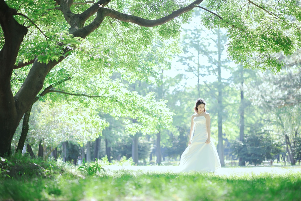 新緑の木漏れ日の中に立つウェディングドレスの花嫁。5月の新緑がまぶしい季節に撮る洋装ロケーションフォト