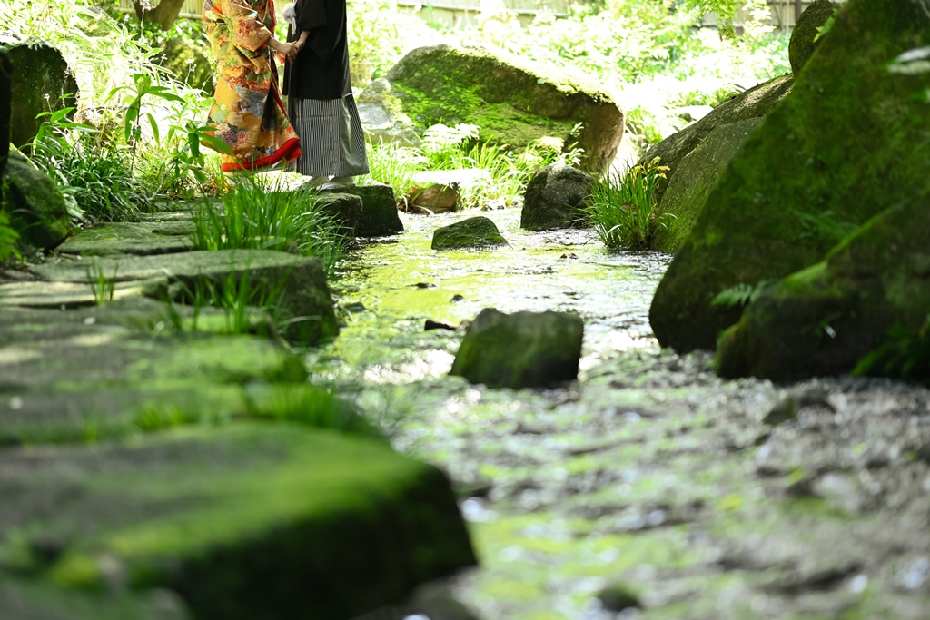 川のほとりで寄り添う紋付袴の新郎と和装の新婦。夏の水辺で撮る涼しげな雰囲気の和装前撮りフォトウェディング